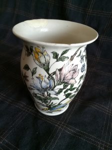 Un vaso in terracotta bianca con decorazioni vegetali e fiori, visto di lato