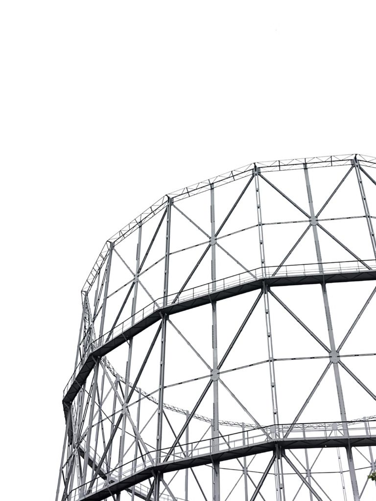 Lo scheletro metallico di un gasometro ripreso guardando verso l'alto, la foto non è in bianco e nero ma il cielo grigio chiaro sullo sfondo la rende quasi tale. La struttura è una serie di travi orizzontali, verticali e diagonali disposta a formare un grande cilindro vuoto.